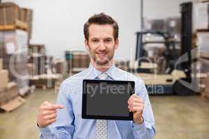 Warehouse manager showing tablet pc smiling at camera