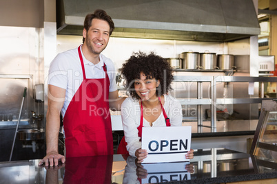 Smiling co-workers posing with open sign