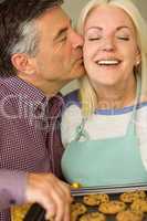 Mature blonde holding fresh cookies with husband kissing her