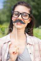 Pretty brunette smiling at camera with fake mustache