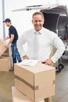 Smiling manager standing behind stack of cardboard boxes