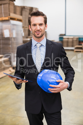 Warehouse manager holding tablet and hard hat