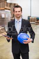 Warehouse manager holding tablet and hard hat