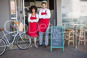 Smiling colleagues in red apron with arms crossed