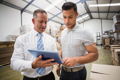 Warehouse manager using tablet pc with colleague