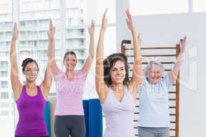 Female friends with arms raised exercising in gym