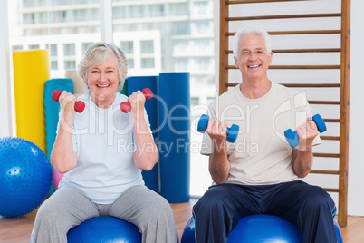 Happy senior couple lifting dumbbells on exercise ball