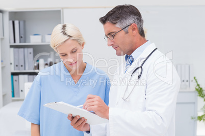Doctor and nurse discussing over notes on clipboard