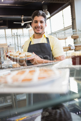 Smiling worker showing plate of cupcakes