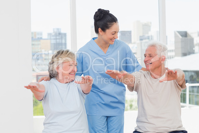 Female trainer assisting senior couple to exercise