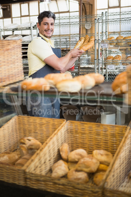 Cheerful waiter in apron holding baguettes