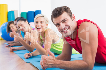 Friends gesturing thumbs up while lying on mats at gym