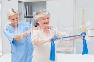 Nurse assisting senior patient in exercising with resistance ban