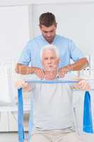 Physiotherapist assisting senior man in exercising with resistan