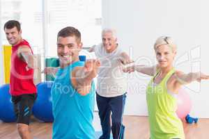 Happy people doing warrior pose in yoga class