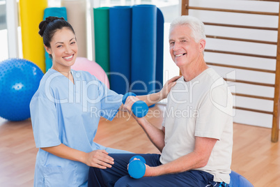 Female instructor with senior man lifting dumbbells