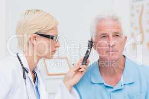 Doctor examining male patients ear with otoscope