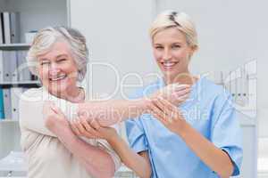 Smiling nurse assisting senior patient in raising arm