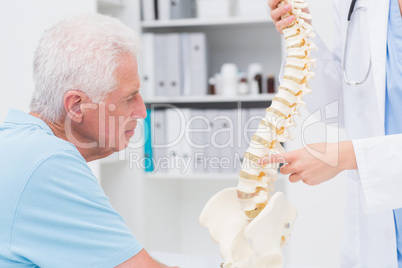 Doctor explaining anatomical spine to senior man