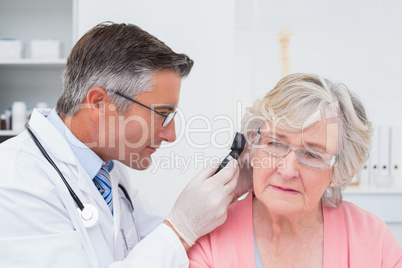 Doctor examining female patients ear with otoscope