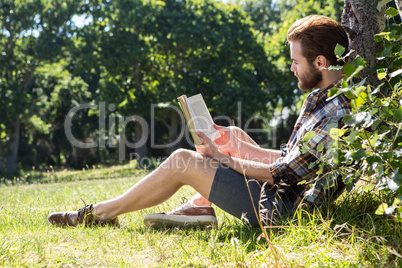 Handsome hipster reading book in park