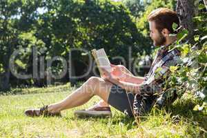 Handsome hipster reading book in park