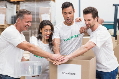 Volunteer team holding hands on a box of donations