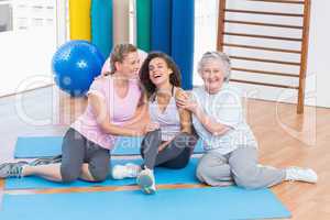 Playful friends sitting on exercise mat in gym
