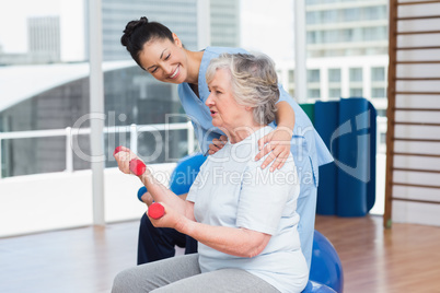 Trainer looking at senior woman lifting dumbbells