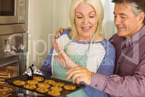 Woman taking tray of fresh cookies out of oven with husband