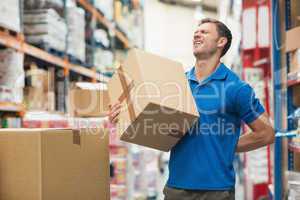 Worker with backache while lifting box in warehouse