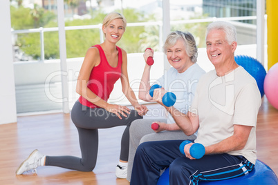 Happy senior couple lifting dumbbells by trainer