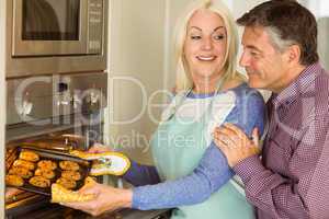 Woman taking tray of fresh cookies out of oven with husband