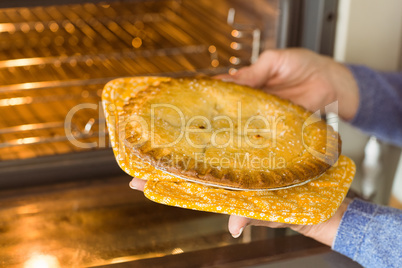 Woman taking fresh pie out of oven