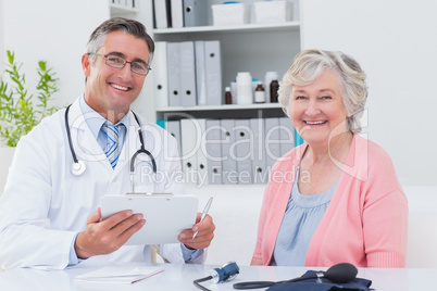 Doctor holding clipboard while sitting with senior patient Doctor holding clipboard while sitting with senior patient