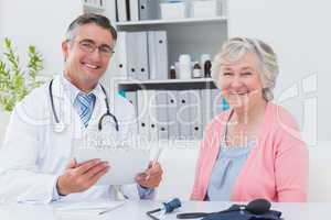 Doctor holding clipboard while sitting with senior patient