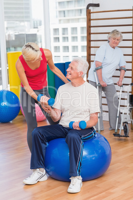 Trainer assisting senior man in lifting dumbbells