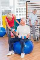 Trainer assisting senior man in lifting dumbbells