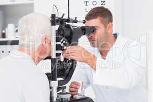 Optometrist examining senior mans eyes through slit lamp