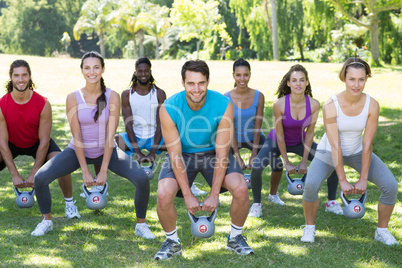 Fitness group squatting in park with kettle bells