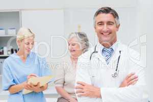 Doctor standing arms crossed with nurse and patient in backgroun