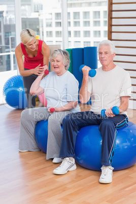 Trainer motivating senior couple in lifting dumbbells