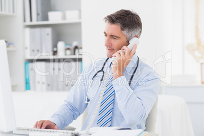 Doctor using telephone while working on computer