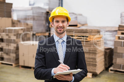 Smiling warehouse manager writing on clipboard