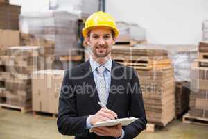 Smiling warehouse manager writing on clipboard