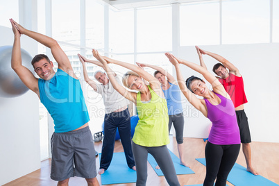 Happy people doing stretching exercise in yoga class