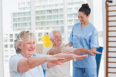 Female instructor assisting senior couple to exercise