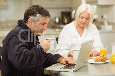 Mature couple having breakfast together man using laptop