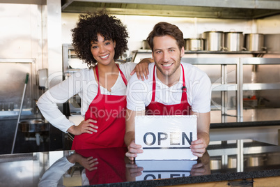 Happy colleagues posing with open sign