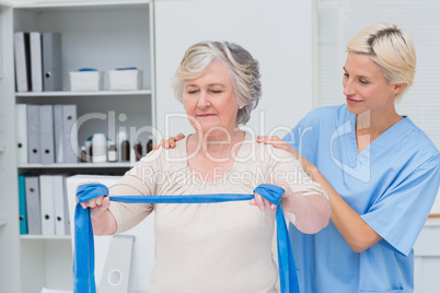 Nurse helping senior patient in exercising with resistance band